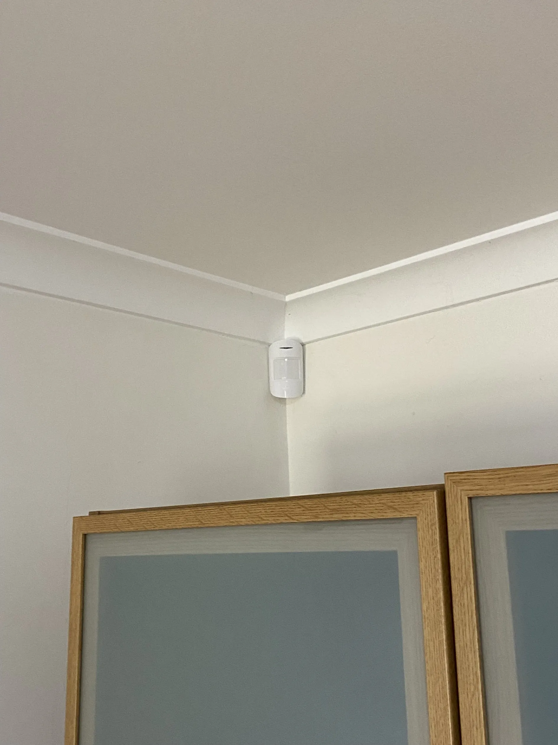 Wireless PIR motion detector neatly installed in a room corner with no visible cabling